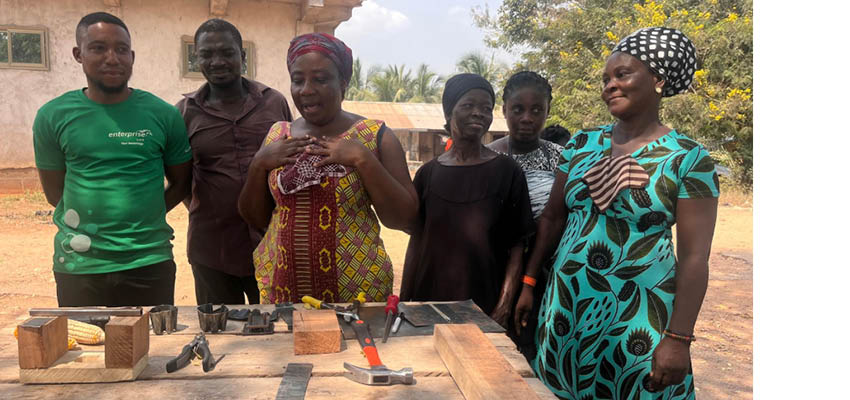 Five people stand behind a work table outside with tools laid out on it.