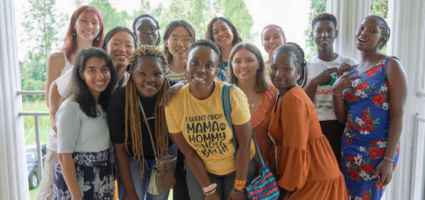 Thirteen smiling women standing, smiling for a photograph.