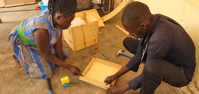 Woman crouching and man sitting on the ground together putting together a wooden frame.